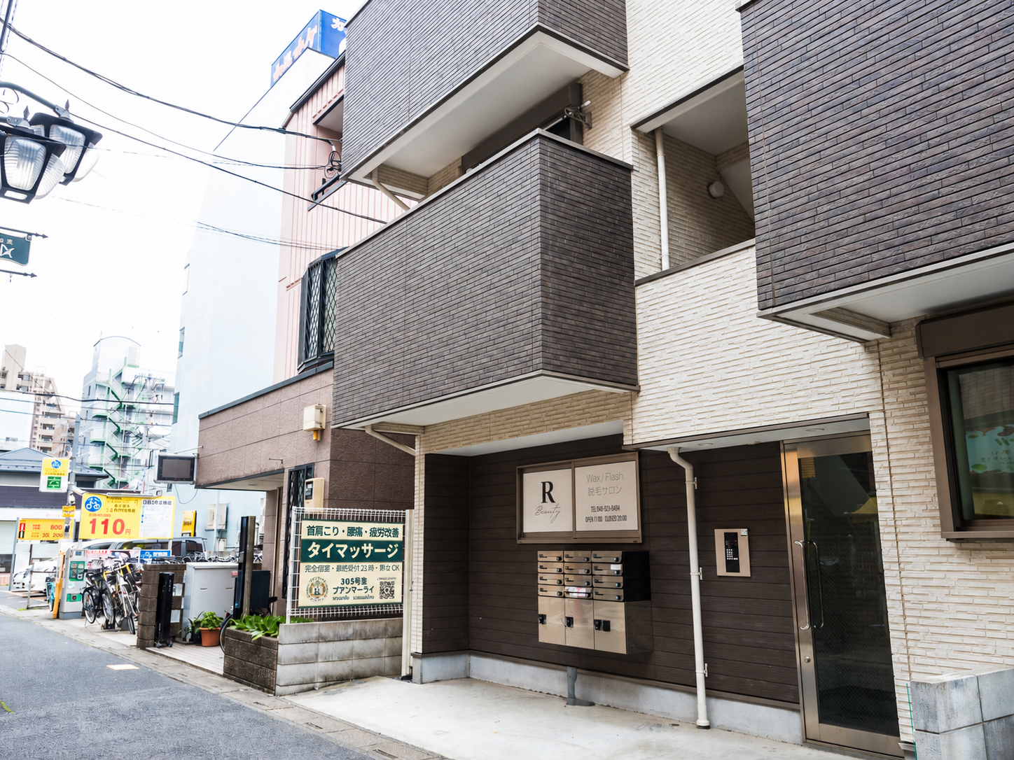フェンスのプアンマーライの看板と、ウエストガーデン草加氷川の建物・入口